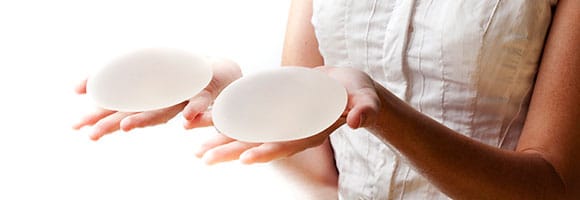 woman holding two hands out with silicone breast implant in each