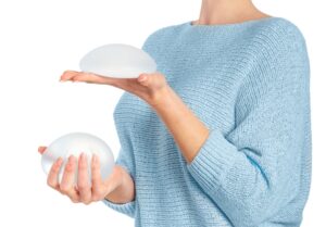 Woman who previously had a breast augmentation holds new breast implants in her hand when considering breast revision surgery.