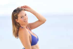 Woman in blue bikini on the beach takes her sunglasses off to enjoy the beach.