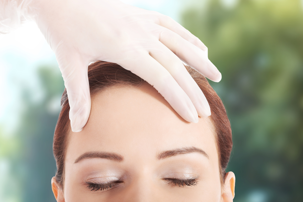 Doctor's gloved hand rests on a woman's rejuvenated forehead.